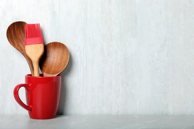 Photo of Set of wooden kitchen utensils in red cup on light grey table. Space for text