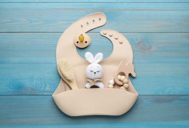 Photo of Silicone baby bib, toys and accessories on light blue wooden background, flat lay