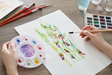 Photo of Man painting flowers with watercolor at wooden table, closeup. Creative artwork