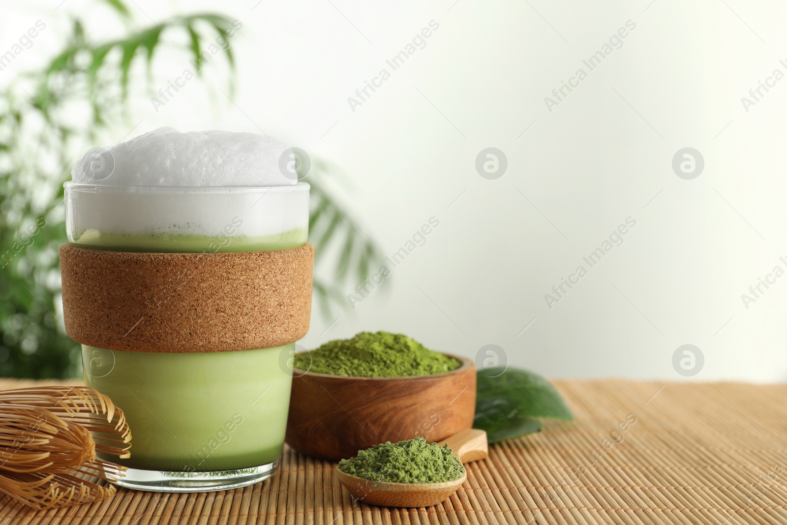 Photo of Glass cup of fresh matcha latte, powder and bamboo whisk on table. Space for text