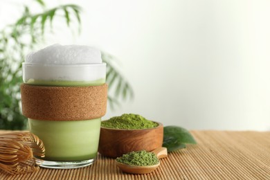 Photo of Glass cup of fresh matcha latte, powder and bamboo whisk on table. Space for text