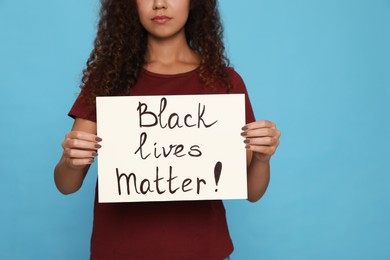 African American woman holding sign with phrase Black Lives matter on light blue background, closeup. Racism concept