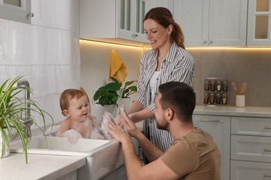 Photo of Father and mother washing their little baby in sink at home
