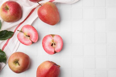 Photo of Tasty apples with red pulp and leaves on white tiled table, flat lay. Space for text