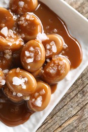 Tasty candies, caramel sauce and salt on wooden table, top view