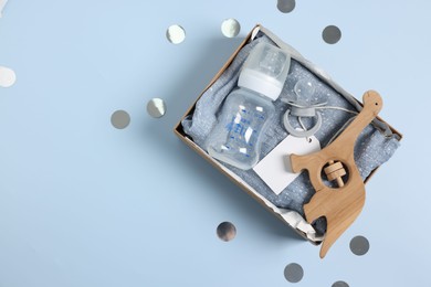 Photo of Different baby accessories with blank card in box and confetti on light blue background, top view. Space for text
