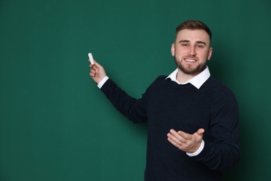 Photo of Portrait of young teacher with chalk on green background. Space for text