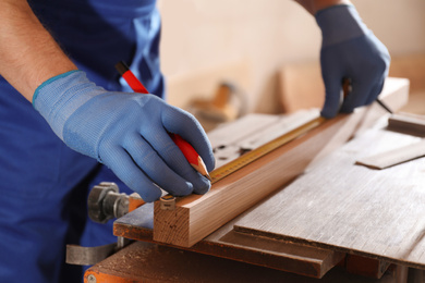 Photo of Professional carpenter measuring wooden bar in workshop, closeup