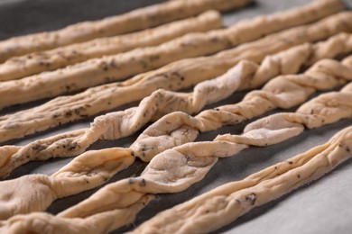Photo of Homemade breadsticks with spices on baking sheet, closeup. Cooking traditional grissini