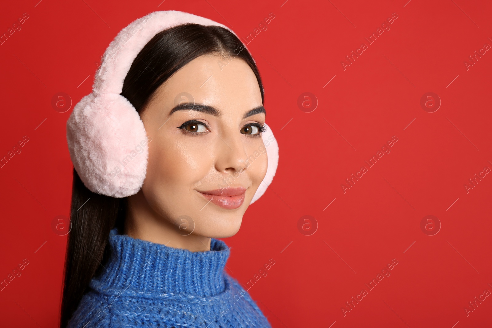 Photo of Beautiful young woman wearing earmuffs on red background. Space for text