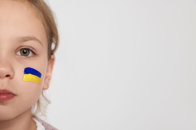 Photo of Little girl with drawing of Ukrainian flag on face against white background, closeup. Space for text