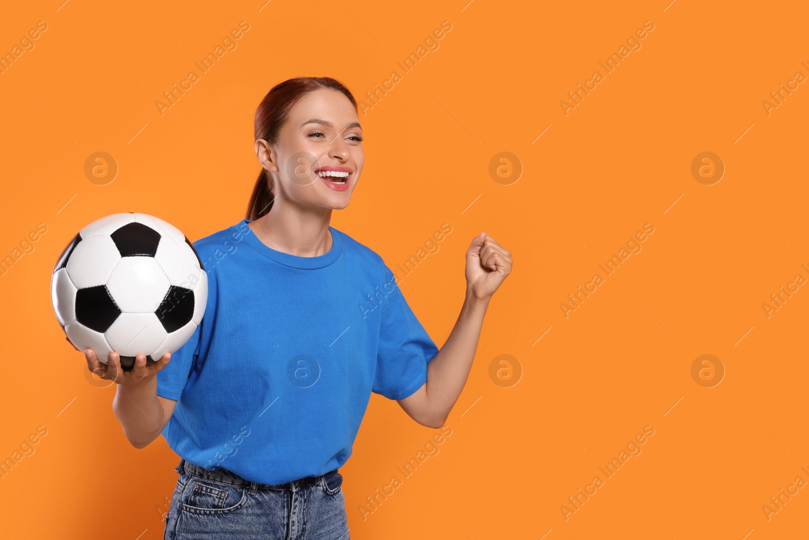 Photo of Happy fan with football ball on orange background, space for text