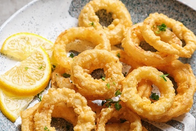 Homemade crunchy fried onion rings and lemon slices on plate, closeup