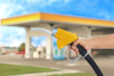 Man holding fuel nozzle against blurred gas station, closeup