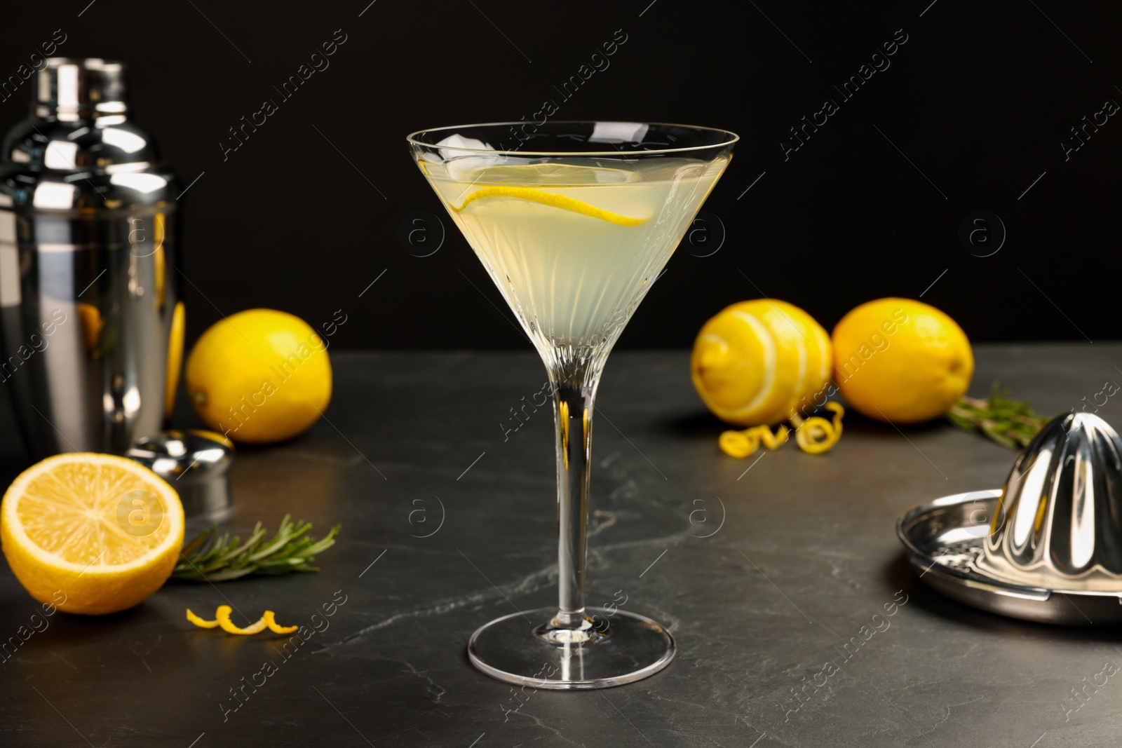 Photo of Martini glass of refreshing cocktail with lemon slice, fresh fruits, rosemary, shaker and hand citrus squeezer on black table