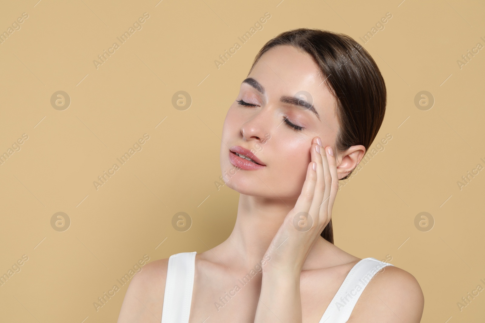 Photo of Young woman applying cream under eyes on beige background, space for text