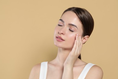 Young woman applying cream under eyes on beige background, space for text