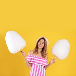 Photo of Happy young woman with cotton candies on yellow background