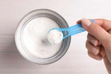 Photo of Woman taking powdered infant formula with scoop from can at white wooden table, top view