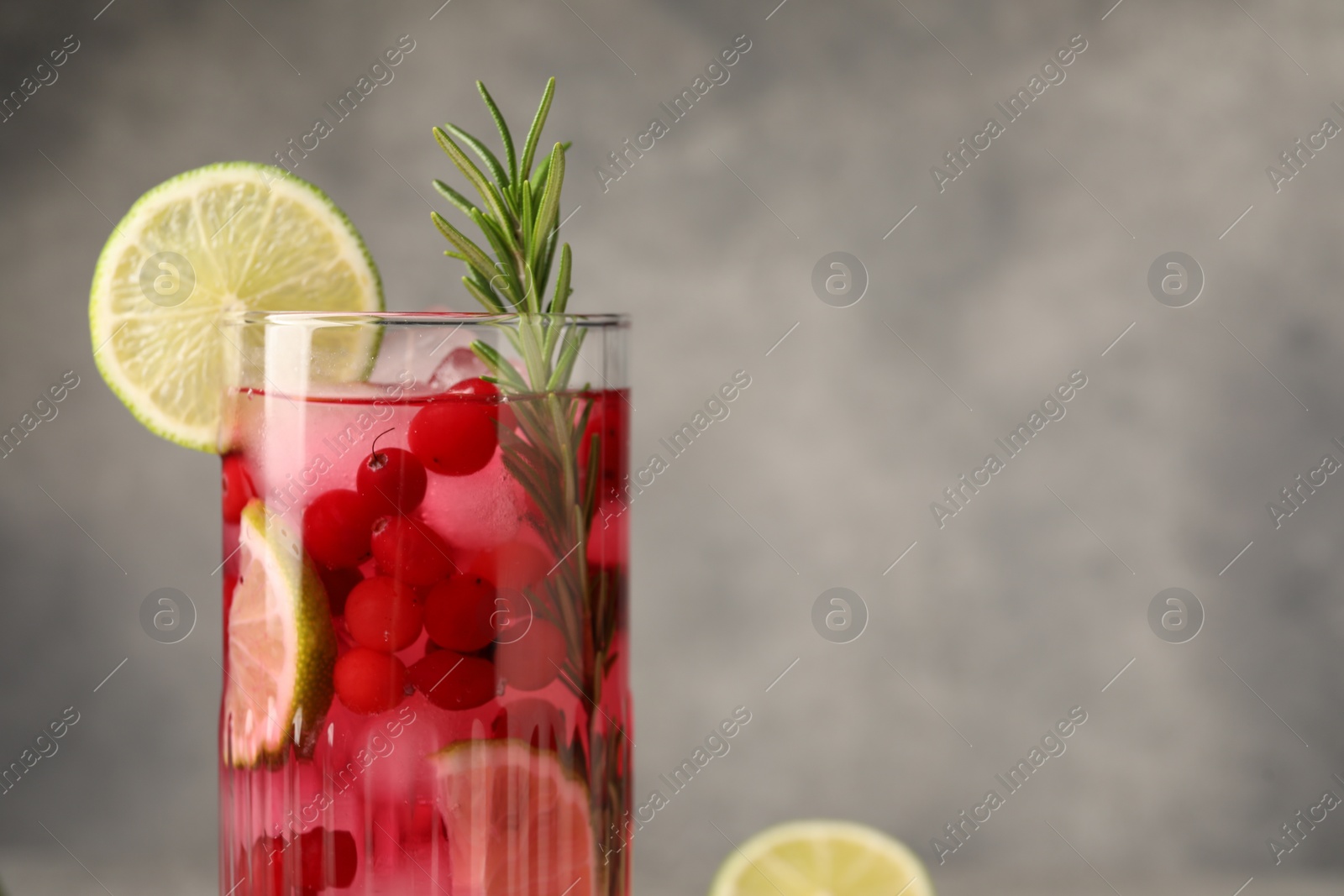 Photo of Tasty cranberry cocktail with rosemary and lime in glass on gray background, closeup. Space for text