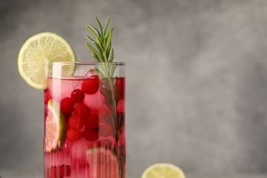 Tasty cranberry cocktail with rosemary and lime in glass on gray background, closeup. Space for text