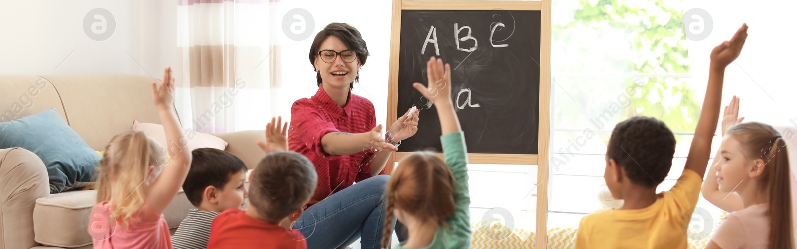 Image of Young nanny teaching little children indoors. Banner design 