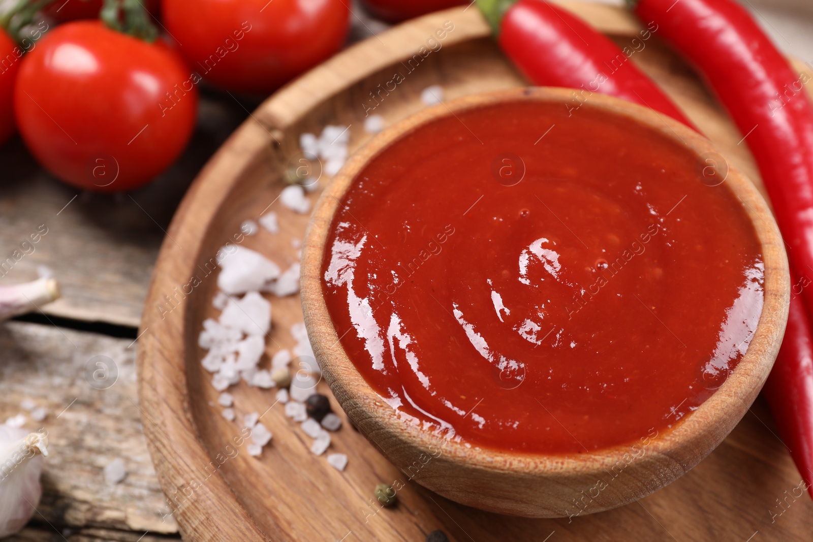 Photo of Delicious ketchup in bowl, chili pepper and spices on wooden table, closeup. Tomato sauce