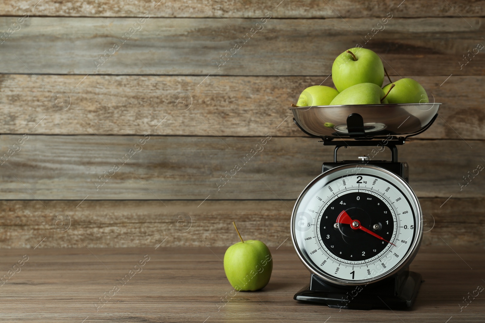 Photo of Kitchen scale with green apples on wooden table. Space for text