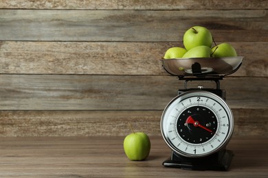 Kitchen scale with green apples on wooden table. Space for text