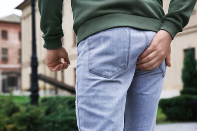 Photo of Man suffering from hemorrhoid pain outdoors, back view