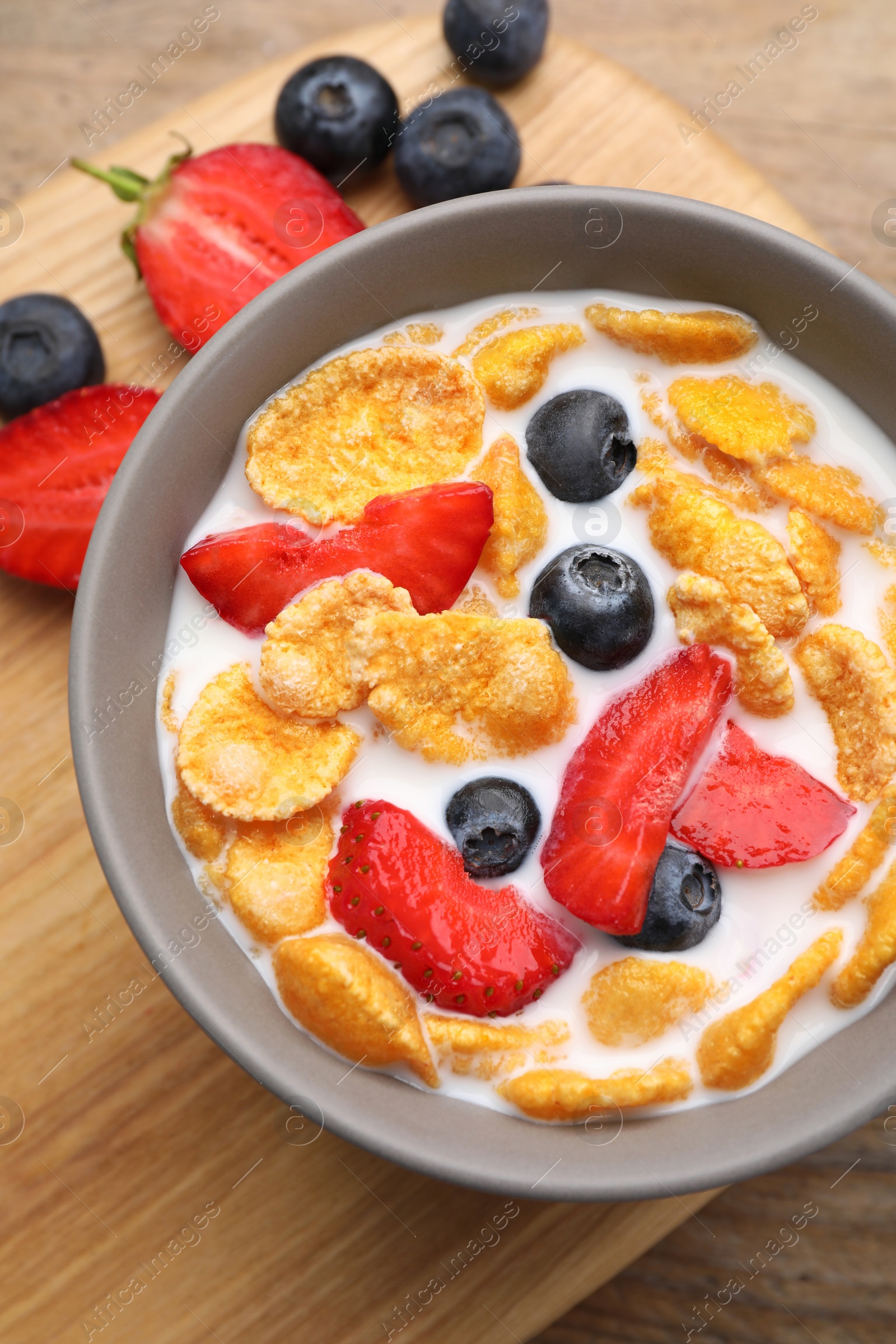 Photo of Bowl of tasty crispy corn flakes with milk and berries on wooden table, flat lay