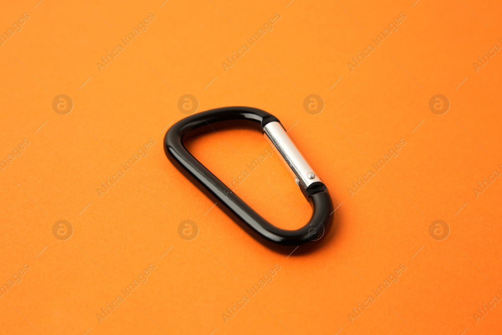 Photo of One black carabiner on orange background, closeup