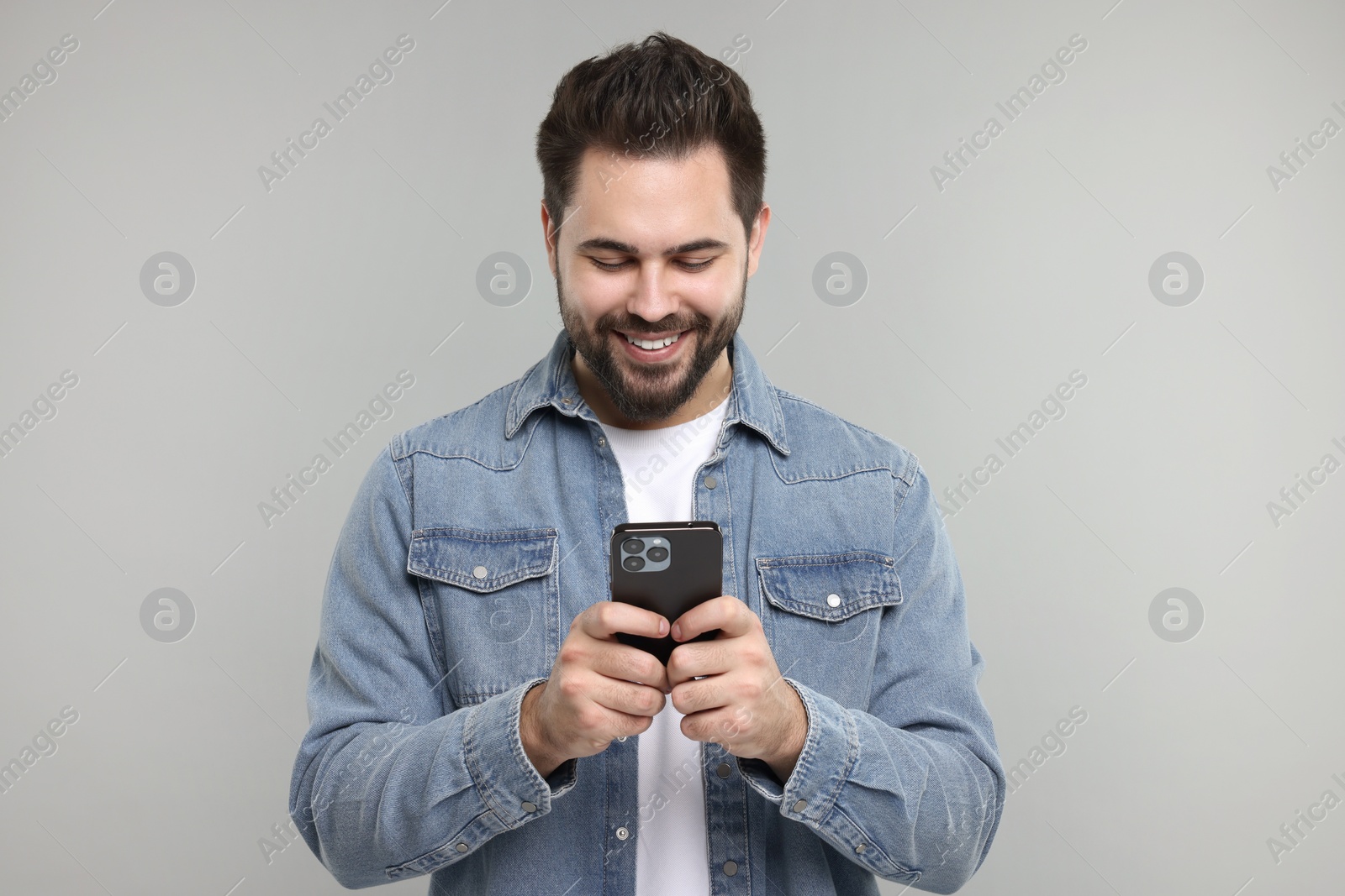 Photo of Happy young man using smartphone on grey background