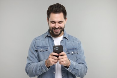 Happy young man using smartphone on grey background