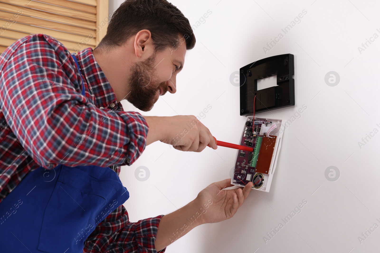 Photo of Technician installing home security alarm system on white wall indoors