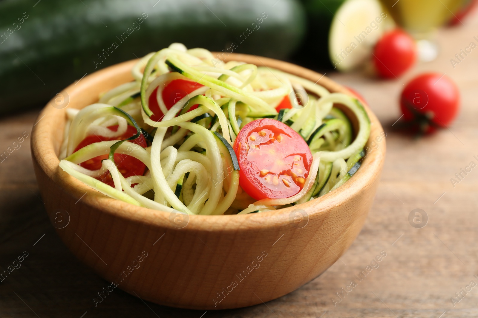 Photo of Delicious zucchini pasta with cherry tomatoes in bowl on wooden table, closeup