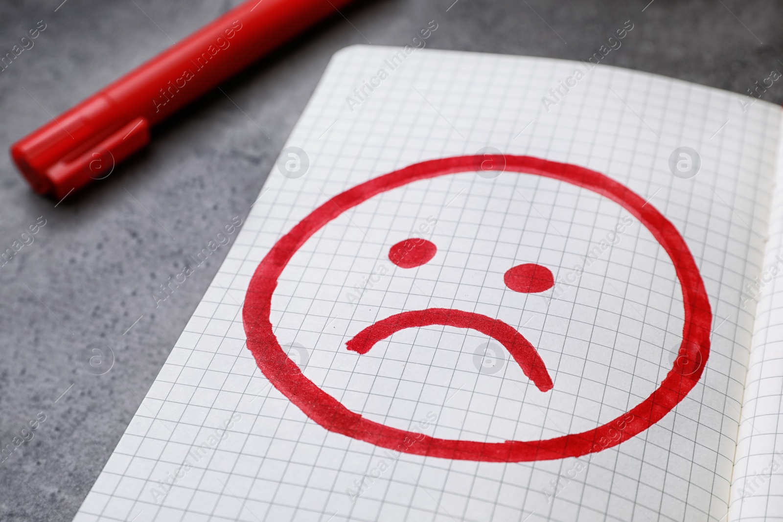 Photo of Notebook with drawing of unhappy face on table, closeup. Depression symptoms