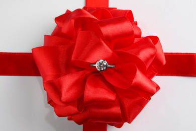 Photo of Beautiful red bow and engagement ring on white background, top view