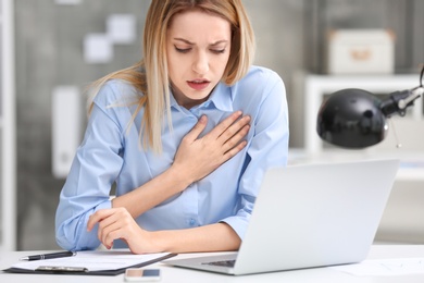 Photo of Young woman suffering from chest pain in office