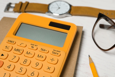 Photo of Calculator, notebook, watch and glasses on white wooden table, closeup. Tax accounting