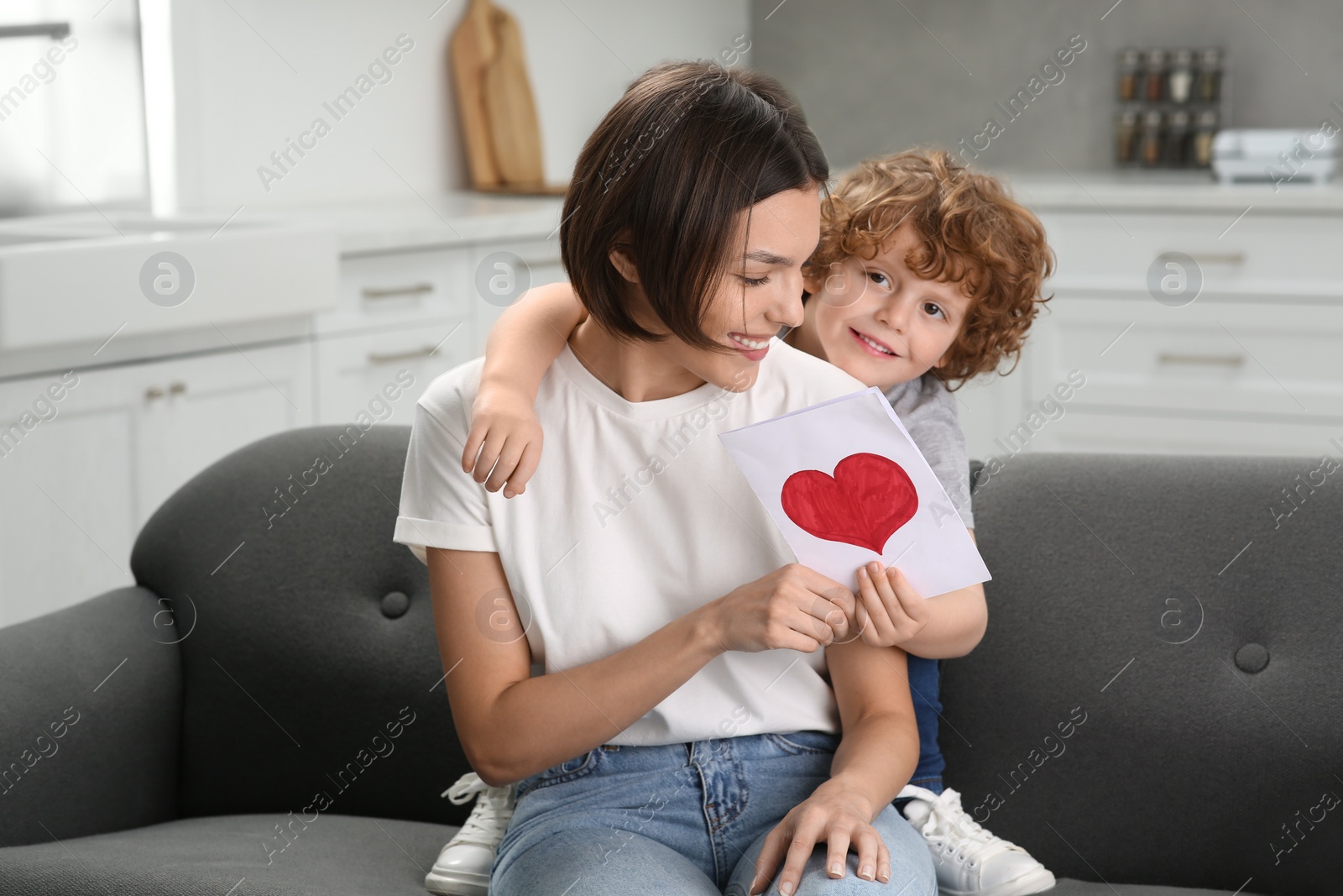 Photo of Little son congratulating his mom with Mother`s day at home. Woman holding greeting card