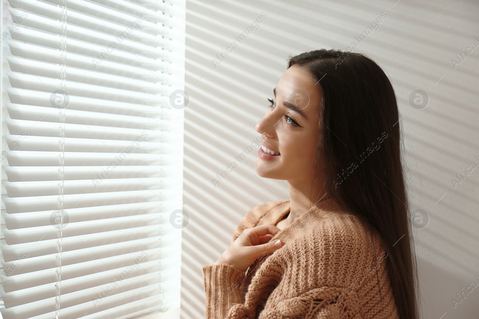 Photo of Young woman near window with Venetian blinds. Space for text