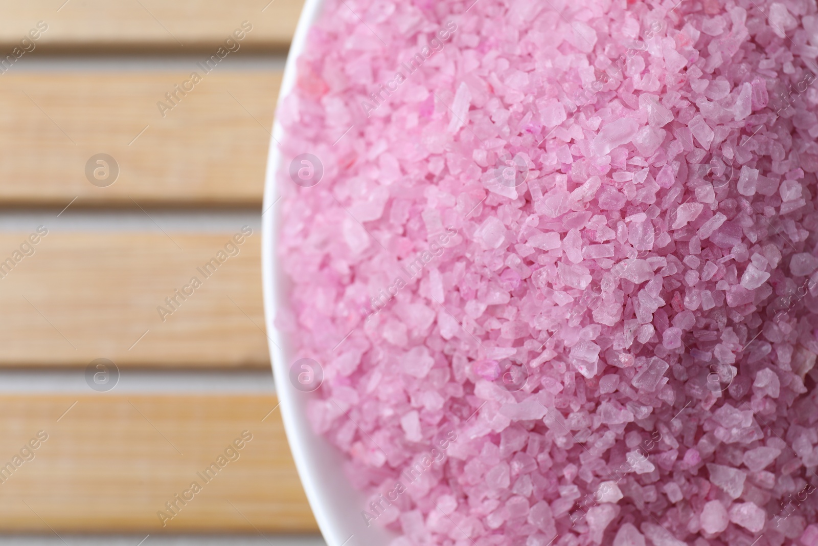 Photo of Bowl with pink sea salt on wooden table, top view