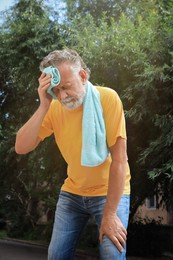 Photo of Senior man with towel suffering from heat stroke outdoors