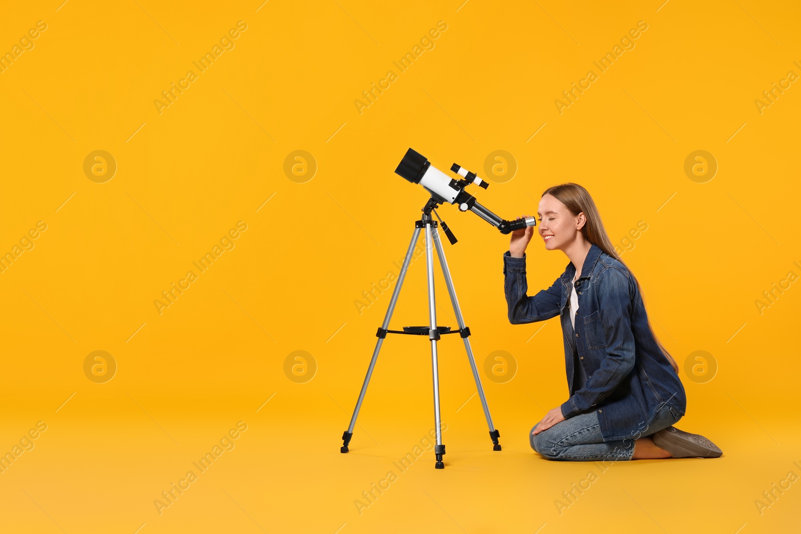 Photo of Young astronomer looking at stars through telescope on orange background, space for text