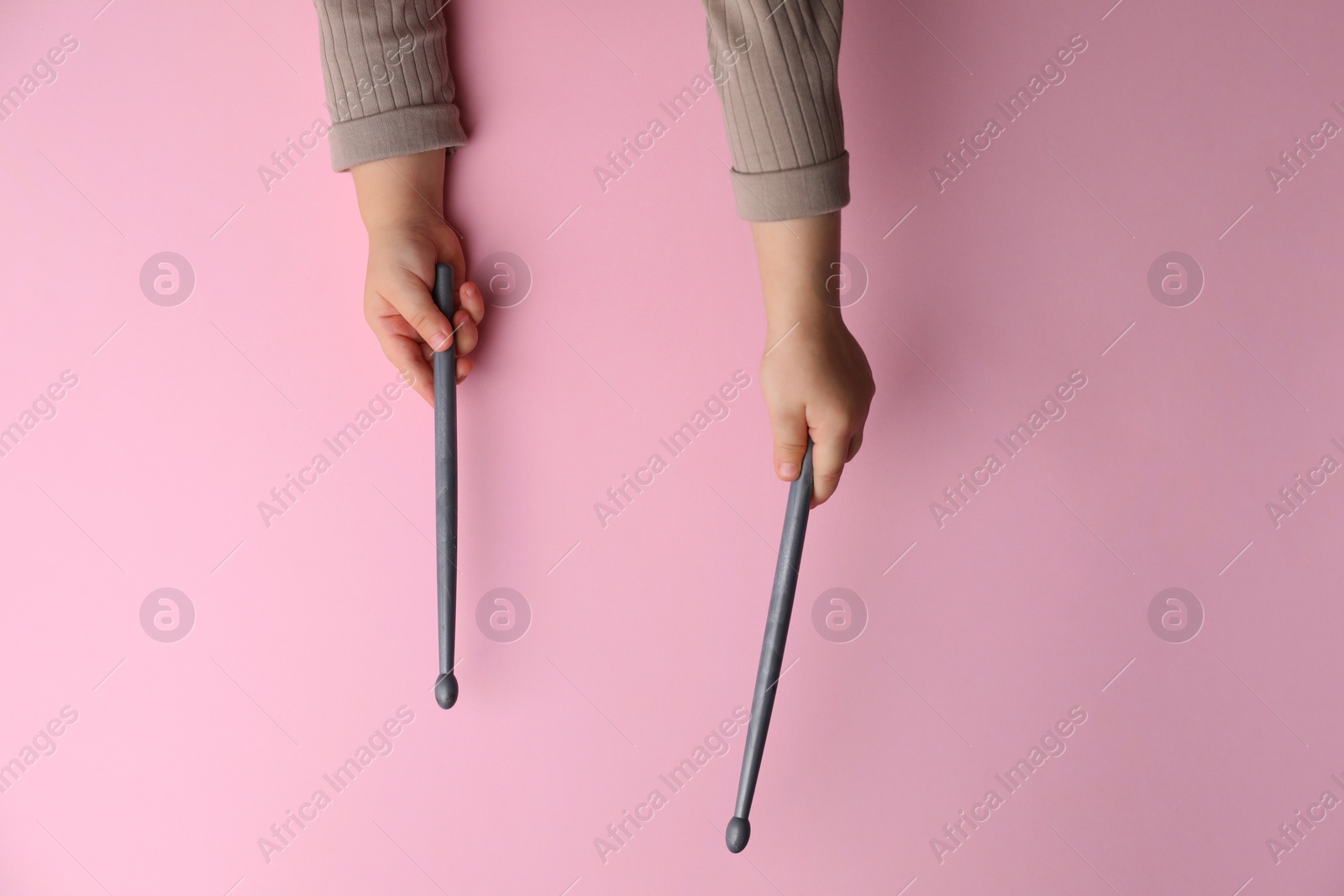 Photo of Little kid holding drumsticks on pink background, top view