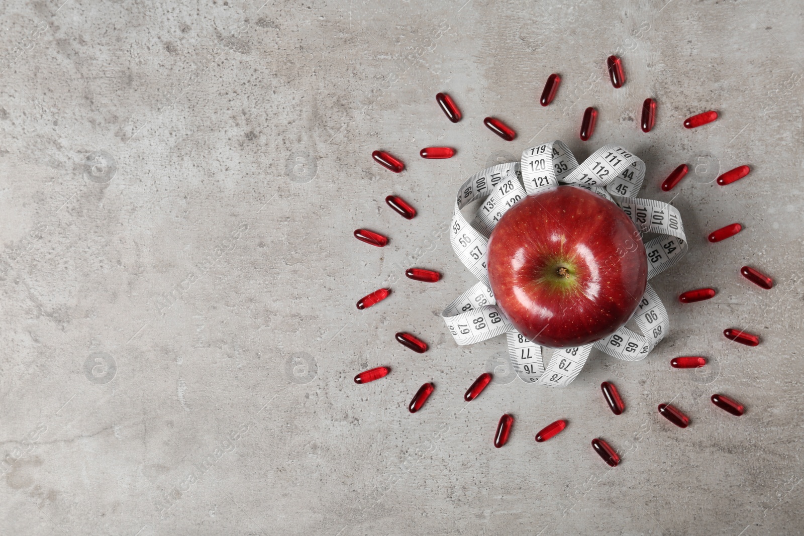 Photo of Weight loss pills with apple and measuring tape on grey background, flat lay. Space for text