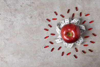 Photo of Weight loss pills with apple and measuring tape on grey background, flat lay. Space for text