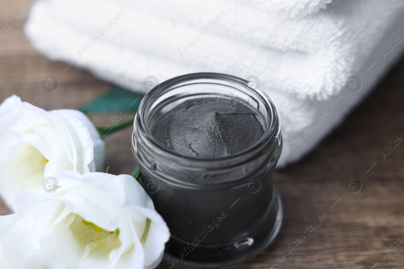 Photo of Folded towels, jar of cosmetic mask and eustoma flowers on wooden table