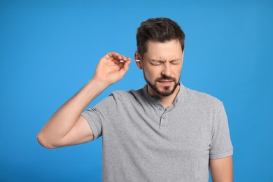 Man cleaning ears and suffering from pain on light blue background